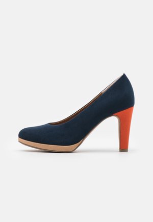 Zapato de tacón alto de ante azul marino con punta redonda, que presenta un tacón naranja en contraste y una plataforma beige. Textura suave en todo el zapato.