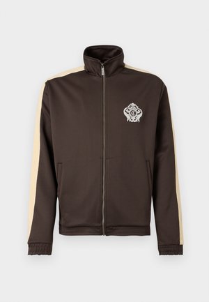 Veste zippée marron foncé avec des rayures beiges sur les manches et un emblème blanc orné sur la poitrine gauche, dotée d'un col montant et de poches latérales.