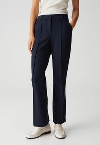 Marineblauwe op maat gemaakte broek met een gladde textuur, rechte pasvorm en voorplooi detail. Draagt met lichtgekleurde instappers.