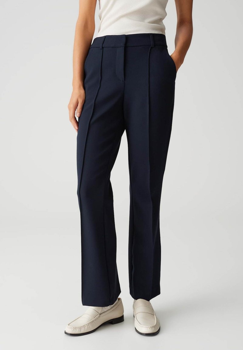 Marineblauwe op maat gemaakte broek met een gladde textuur, rechte pasvorm en voorplooi detail. Draagt met lichtgekleurde instappers.