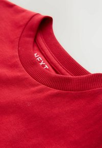 Red cotton T-shirt with a ribbed crew neck. The fabric appears smooth with a slight texture. Brand label shown inside collar.