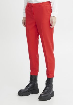Red tailored pants with a slim fit, made of smooth fabric, featuring side pockets, and worn with black lace-up combat boots.