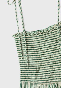 Robe à rayures vertes et crème avec corsage froncé et bordure à volants. Dispose de fines bretelles ajustables et d'un tissu texturé.