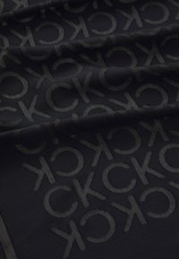 Tessuto nero con motivo in rilievo delle lettere "CK" ripetuto in tutta la superficie. Texture liscia con una leggera lucentezza. I bordi sono rifiniti in modo impeccabile.