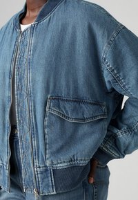 Jeans-Bomberjacke in Hellblau mit geripptem Kragen und Bündchen. Verfügt über einen Frontreißverschluss und eine Seitentasche in der Nähe. Strukturierter Stoff.