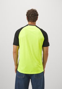 Maglietta sportiva a maniche corte di colore giallo neon con maniche raglan nere e scollatura rotonda, caratterizzata da una texture liscia e dettaglio del logo.