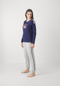 Granatowy sweter z grafiką na przodzie, w zestawieniu z szarymi dresami z bocznym paskiem i elastycznymi mankietami.