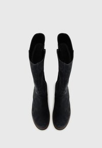 Bottes noires en suede montantes avec une texture lisse, des zips sur le côté et un design de bout légèrement pointu. Intérieur doublé pour le confort.