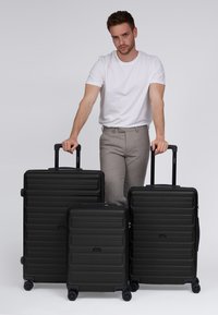 Drei schwarze Hartschalenkoffer in unterschiedlichen Größen, mit strukturierten Oberflächen, horizontalen Linien und multidirektionalen Rollen.