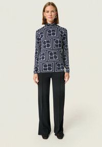 Langærmet turtleneck top i marineblå med hvidt geometrisk mønster; parret med sorte vide bukser; glat stof, afslappet pasform.