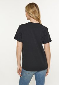 Sort kortærmet T-shirt lavet af bomuld, med en rund halsudskæring og foldede ærmer. Bagfra ses en afslappet pasform og glat tekstur.
