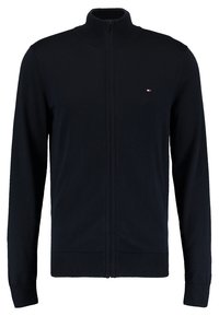 Námořnická svetr s vínkem na zip vyrobený z pletené textilie, s vysokým límcem, žebrovanými manžetami a malým logem na hrudi.