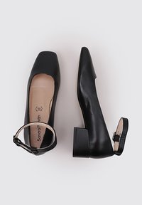 Chaussures noires en cuir à talons carrés avec un bout carré et une sangle à la cheville. L'intérieur présente une doublure beige avec un logo. Texture lisse dans l'ensemble.