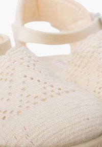 Beige gestrickte Sandalen mit offener Zehenpartie, texturiertem Obermaterial mit Rautenmuster und verstellbarem Knöchelriemen.