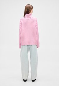 Růžový žebrovaný rolák s volnějším střihem, s nízkými rameny a zaobleným lemem, doplněný světlými širokými džínovými kalhotami.