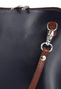 Marineblauwe lederen handtas met een gladde textuur, voorzien van een bruine leren band en zilverkleurige metalen accenten, waaronder een ritssluiting en clips.