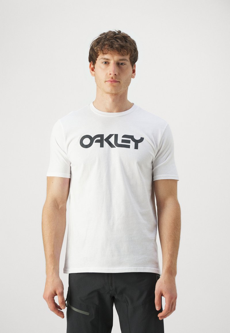 Biała bawełniana koszulka z krótkim rękawem, na której znajduje się duże czarne logo "OAKLEY" z przodu. Posiada okrągły dekolt.