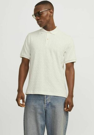 Hvid kortærmet polo-shirt med et struktureret diamantmønster, udstyret med en klassisk krave og en to-knaps placket, parret med lyse denimjeans.
