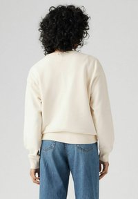 Crème-kleurige sweatshirt met gedropte schouders en geribbelde manchetten, gecombineerd met lichtblauwe denim jeans. Zachte textuur en ontspannen pasvorm.