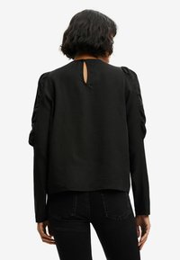 Top noir à manches longues avec un détail en trou de serrure au dos et des accents de manches froncées. Fabriqué en tissu doux avec une coupe décontractée.