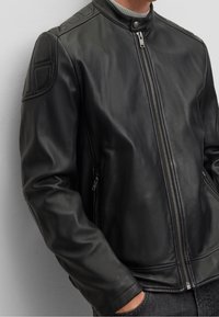 Svart läderjacka med dragkedja fram, ståkrage och kviltade axelpartier. Slät textur och figursydd design med sidofickor med dragkedja.