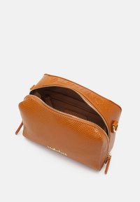 Tan-färgad läderväska med guldfärgade detaljer. Har dragkedjestängning, innerfack och prägling på framsidan.