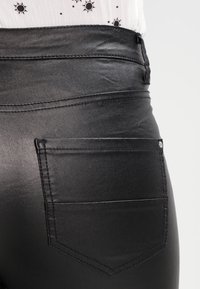 Pantaloni neri aderenti realizzati in materiale lucido. Presentano una tasca posteriore singola con cuciture curve e una finitura texture.