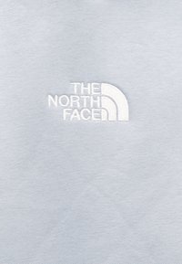 Υφασμάτινο γαλάζιο με κεντημένο λευκό λογότυπο "The North Face" με καμπύλο σχέδιο. Λείο υφή με απλό σχέδιο.