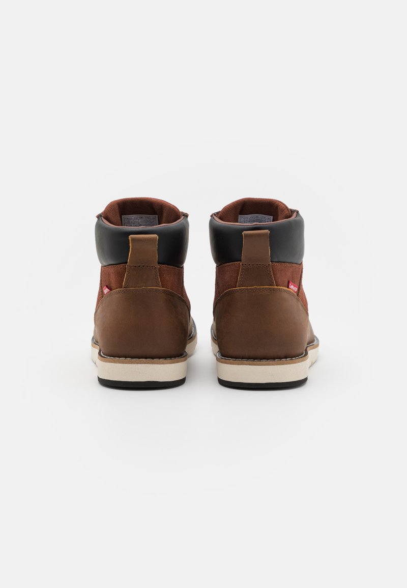 Botas altas de cuero marrón y ante marrón con detalles en negro, que cuentan con un cuello acolchado y una superficie texturizada. Etiqueta de logo roja en el lateral.
