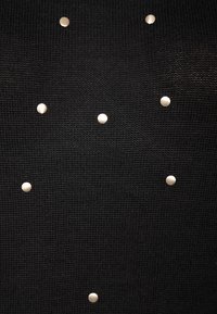 Schwarzer strukturierter Stoff mit metallischen silberfarbenen Nieten, angeordnet in einem Muster. Der Stoff scheint fein gestrickt zu sein.