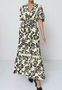 Robe longue et ample en crème avec imprimé floral noir, manches courtes à volants, ceinture à la taille et jupe à volants avec des accents en dentelle.