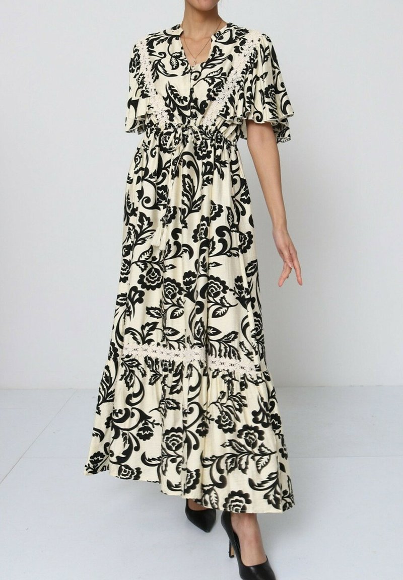 Robe longue et ample en crème avec imprimé floral noir, manches courtes à volants, ceinture à la taille et jupe à volants avec des accents en dentelle.