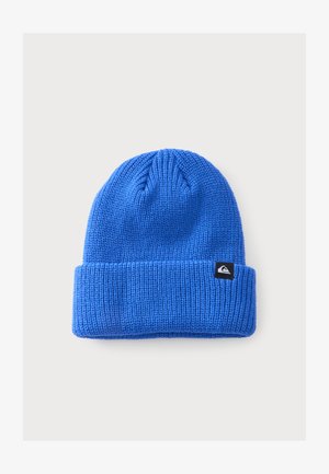 Bonnet en laine bleu tricoté avec un revers plié et une petite étiquette noire avec un logo sur le côté, présenté sur un fond gris clair.