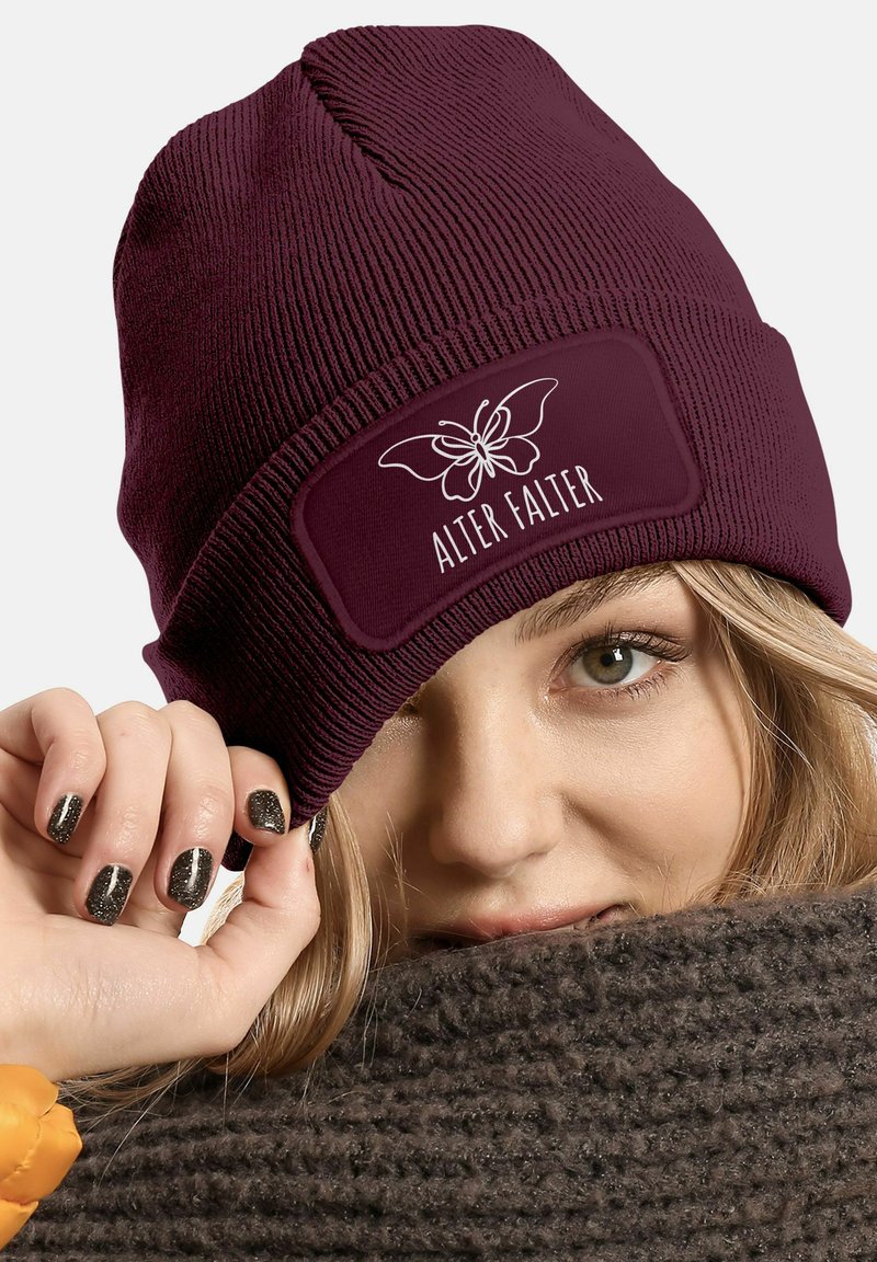 Burgundy knit beanie with a ribbed texture, featuring a rectangular patch with a white butterfly graphic and "ALTER FALTER" text.