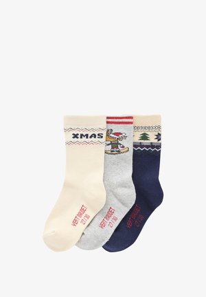 Three pairs of knitted socks: cream with "XMAS," grey with a character design, and navy with a tree pattern, all featuring ribbed cuffs.