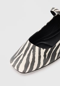 Černobílé baletní boty se zebra vzorem, se čtveratou špičkou, nastavitelným páskem a hladkým černým vnitřním podšívkou. Materiál je z faux kůže.