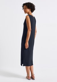 Sleeveless, ribbed, dark navy dress with a high slit and back button detail, featuring a relaxed fit and smooth texture.