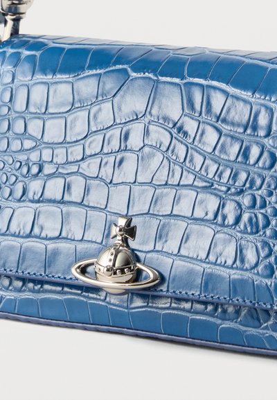 Μπλε δερμάτινο πορτοφόλι με σχέδιο κροκόδειλου και ασημένιο έμβλημα με σφαίρα και σταυρό στο κούμπωμα, σε λευκό φόντο.