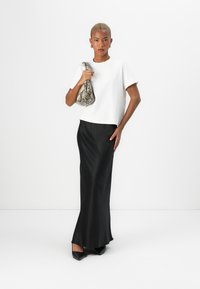 Weißes kurzärmliges Oberteil, schwarer Satin-Maxirock, schwarze High-Heels und eine Handtasche im Schlangenprint. Glatter Stoff und schlichtes Design.