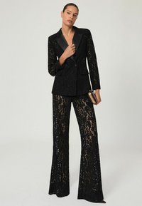 Mustmustreen ülikond, millel on kohandatud bleiser, millel on satiinist krae ja laienevad pükse. Tekstuur on peen ja kaunistatud lillemustritega.