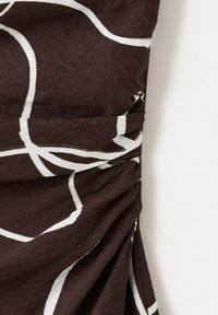 Tissu brun avec des lignes abstraites blanches rassemblées et froncées sur un côté, montrant la texture et les plis sur fond blanc.