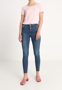 Top rosa claro de manga corta con un sutil patrón de rayas, combinado con jeans skinny azul de tiro alto y zuecos rosas con tacón.