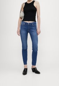 Svart ärmlös topp, blå skinny jeans och svarta klackskor. Anmärkningsvärda detaljer: tygtextur, passform och hög midja.