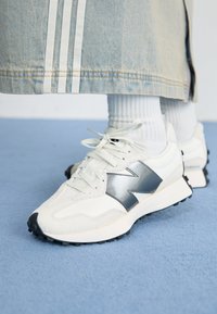 White athletic sneakers with a silver accent, textured fabric and smooth leather; featuring a black rubber sole and laces.