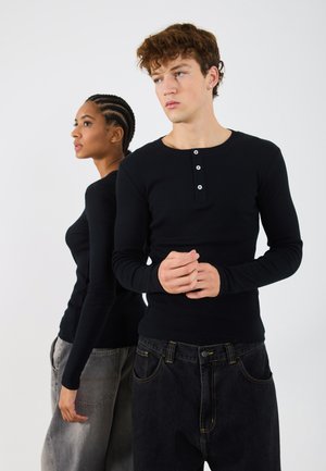 Schwarze langärmelige Henley-Shirts mit Frontknopfdetail, kombiniert mit lockeren schwarzen und grauen Jeans. Glatte Stofftextur, taillierter Schnitt.