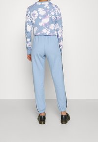 Light blue sweatshirt with floral pattern; matching light blue joggers with side stripes. Soft fabric, relaxed fit, elastic cuffs and waistband.