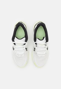 Des chaussures de sport blanches avec des accents noirs et une semelle intérieure vert fluo. Le design présente un dessus texturé et des lacets plats avec un branding prononcé.