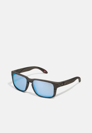 Black sunglasses with square frames, blue reflective lenses, textured arms, and small logo detail on the side.