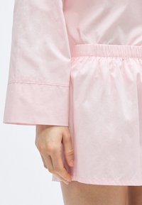 Chemise rose clair à coupe décontractée, avec manches longues, taille élastique et texture lisse et douce.