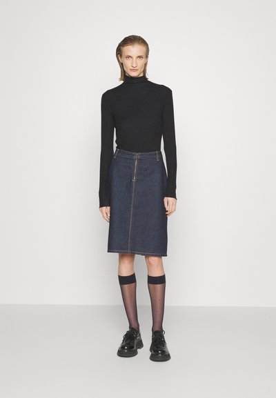 Top negru cu mâneci lungi asociat cu o fustă tip creion din denim de culoare albastră închis, cu fermoar în față și cusături vizibile. Se poartă pantofi negri și șosete până la genunchi.